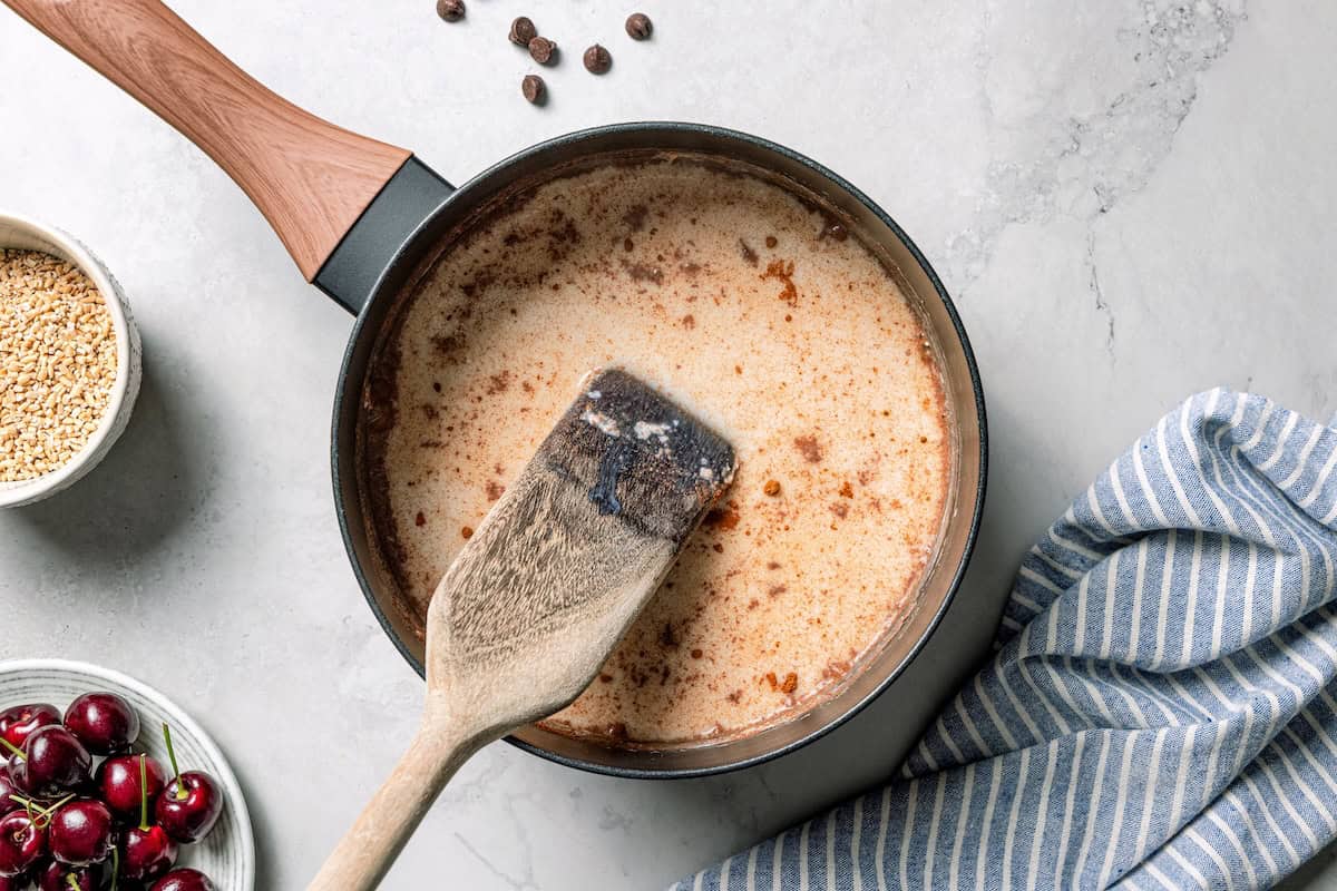 This easy overnight steel-cut oats recipe combines chewy oats, milk, vanilla, and cozy cinnamon into a delicious make-ahead breakfast. Stirring vanilla into a pot of steel cut oats with milk.