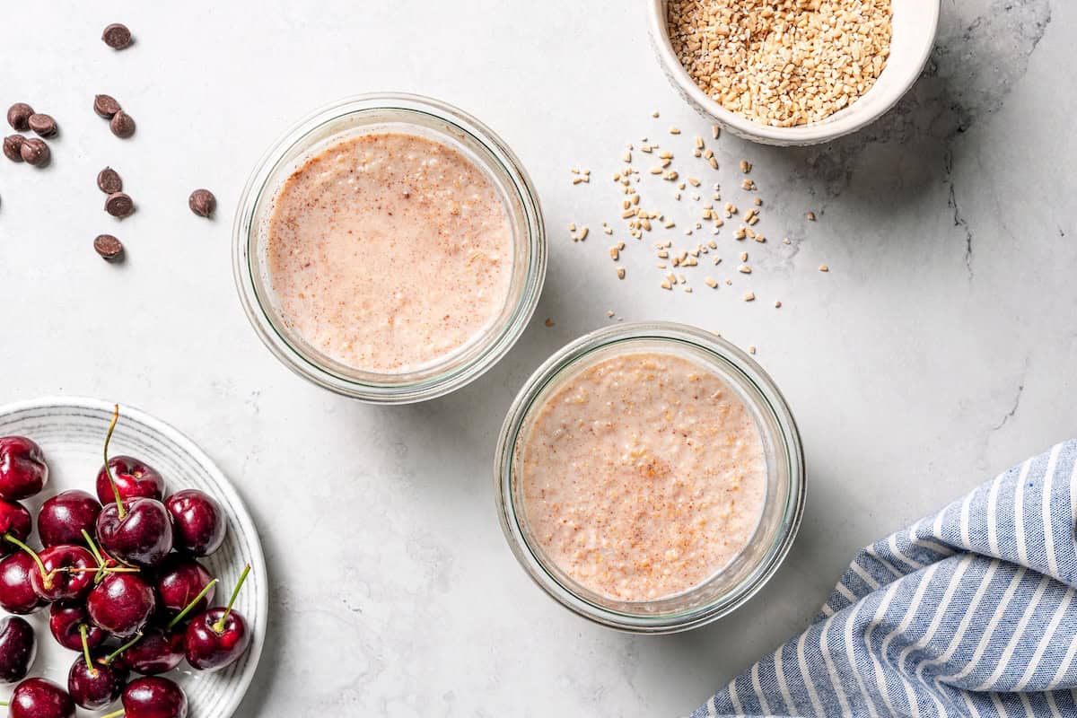 This easy overnight steel-cut oats recipe combines chewy oats, milk, vanilla, and cozy cinnamon into a delicious make-ahead breakfast. Overhead view of steel cut oats mixture added to glass jars.
