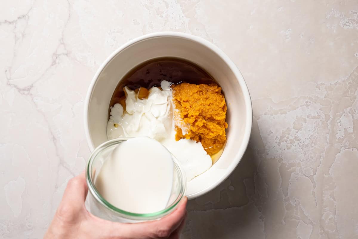 Pumpkin baked oatmeal is the perfect easy, make-ahead fall breakfast! Filled with hearty oats, warm spices, pumpkin purée, and maple syrup. Combining the wet ingredients in a bowl.
