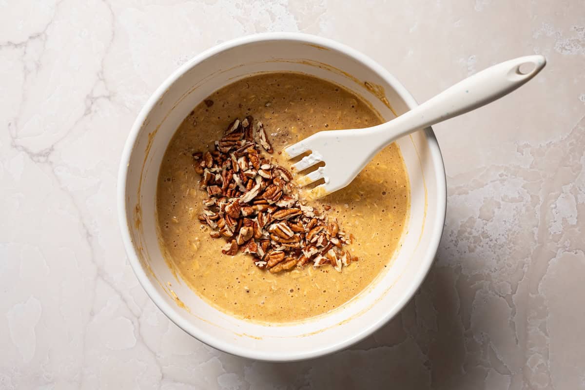 Pumpkin baked oatmeal is the perfect easy, make-ahead fall breakfast! Filled with hearty oats, warm spices, pumpkin purée, and maple syrup. Chopped pecans added to pumpkin oatmeal in a mixing bowl.