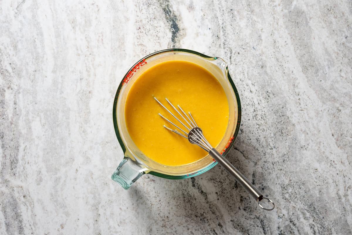 Moist, fluffy pumpkin protein muffins are a high-protein fall treat made with vanilla whey powder, Greek yogurt, eggs, and pumpkin purée. Whisked wet ingredients in a mixing bowl.