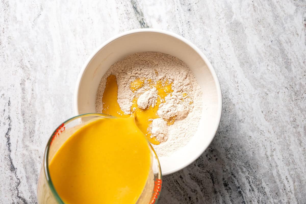 Moist, fluffy pumpkin protein muffins are a high-protein fall treat made with vanilla whey powder, Greek yogurt, eggs, and pumpkin purée. Adding the wet ingredients to dry ingredients in a bowl.