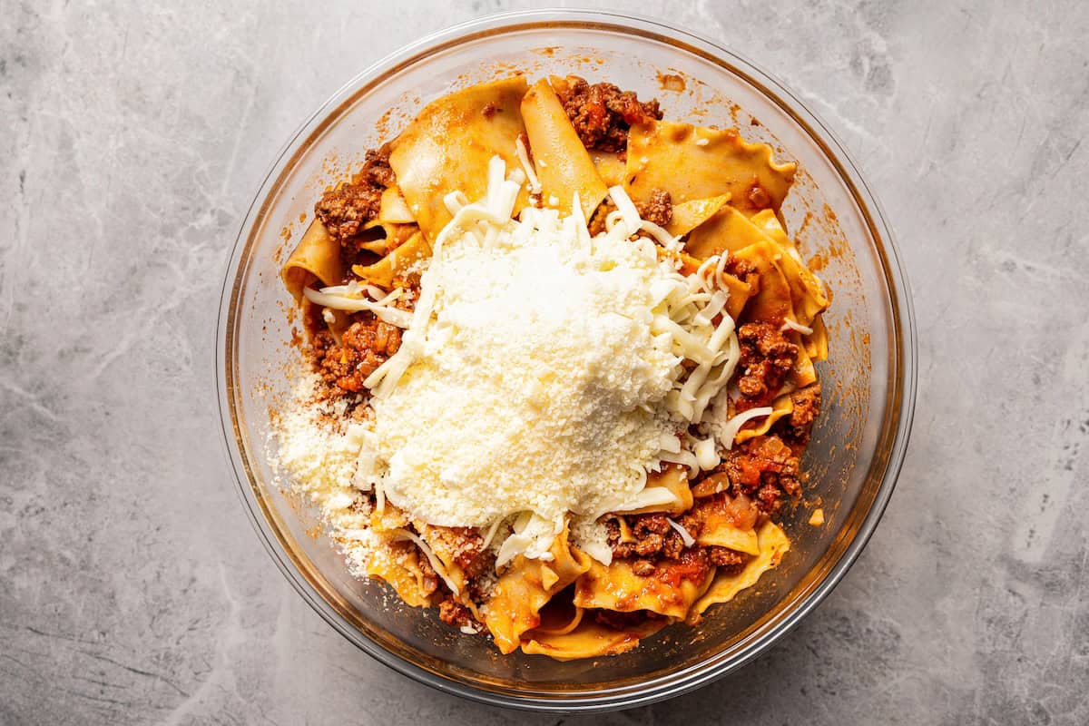 Sheet pan lasagna is a cheesy, delicious, golden-baked lasagna recipe with crispy edges and no layering required. Mix, dump, and bake! Meat sauce, pasta, and cheese combined in a bowl.
