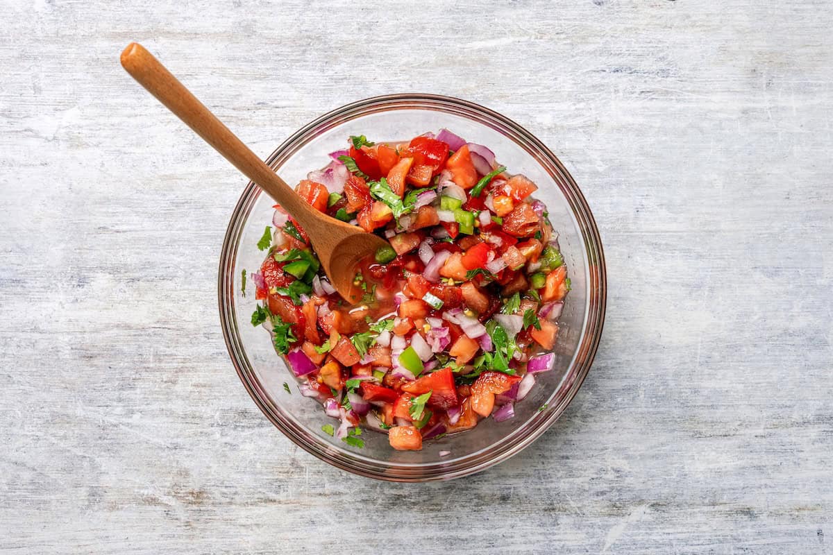 Baked sheet pan tacos are an easy way to make tacos for a crowd with crispy tortillas, seasoned ground beef, melty cheese, and pico de gallo. Homemade pico de gallo in a glass bowl.