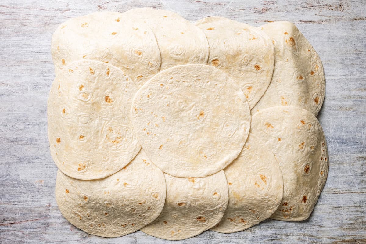 Baked sheet pan tacos are an easy way to make tacos for a crowd with crispy tortillas, seasoned ground beef, melty cheese, and pico de gallo. Flour tortillas arranged on top of a sheet pan.