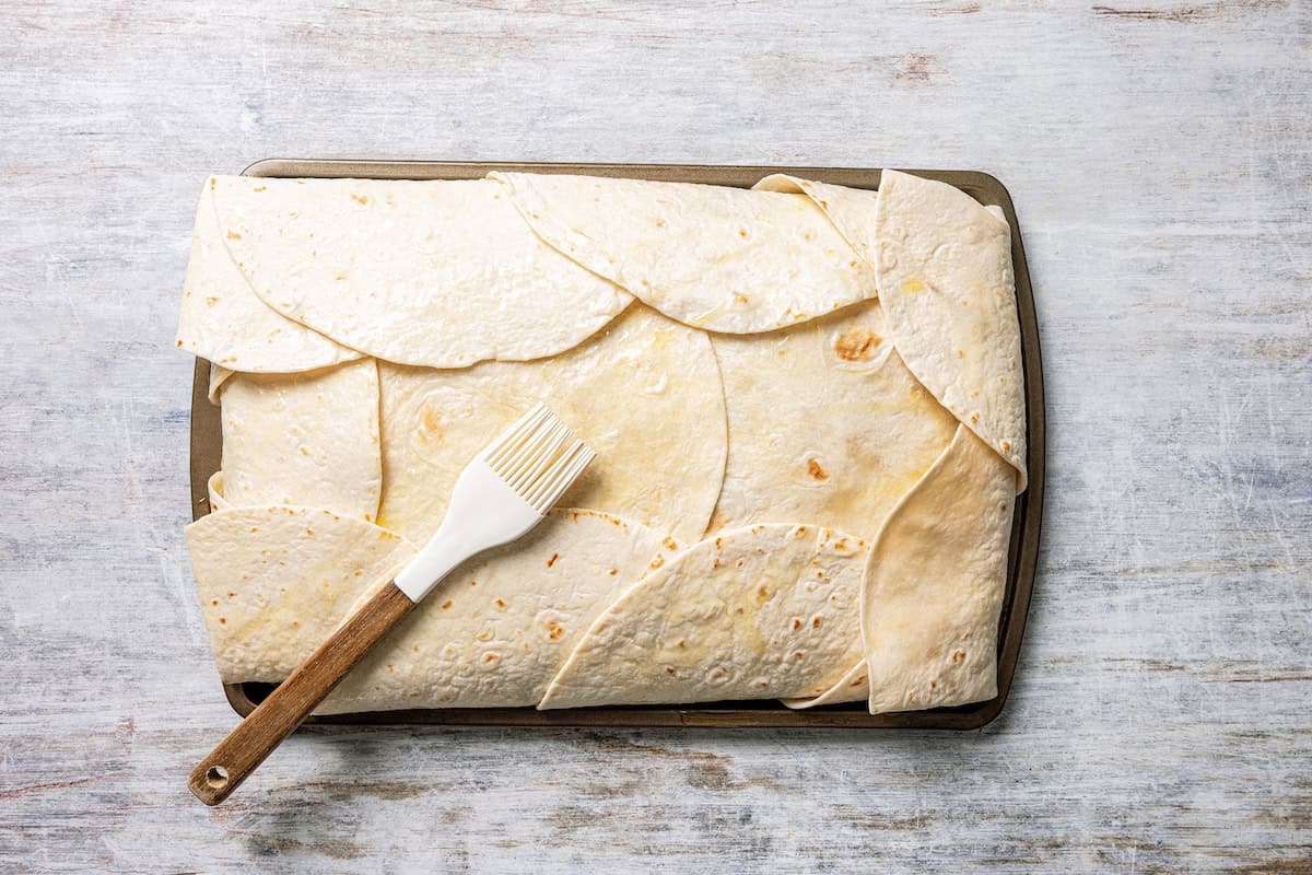 Baked sheet pan tacos are an easy way to make tacos for a crowd with crispy tortillas, seasoned ground beef, melty cheese, and pico de gallo. Flour tortillas folded over beef taco ingredients on a sheet pan.