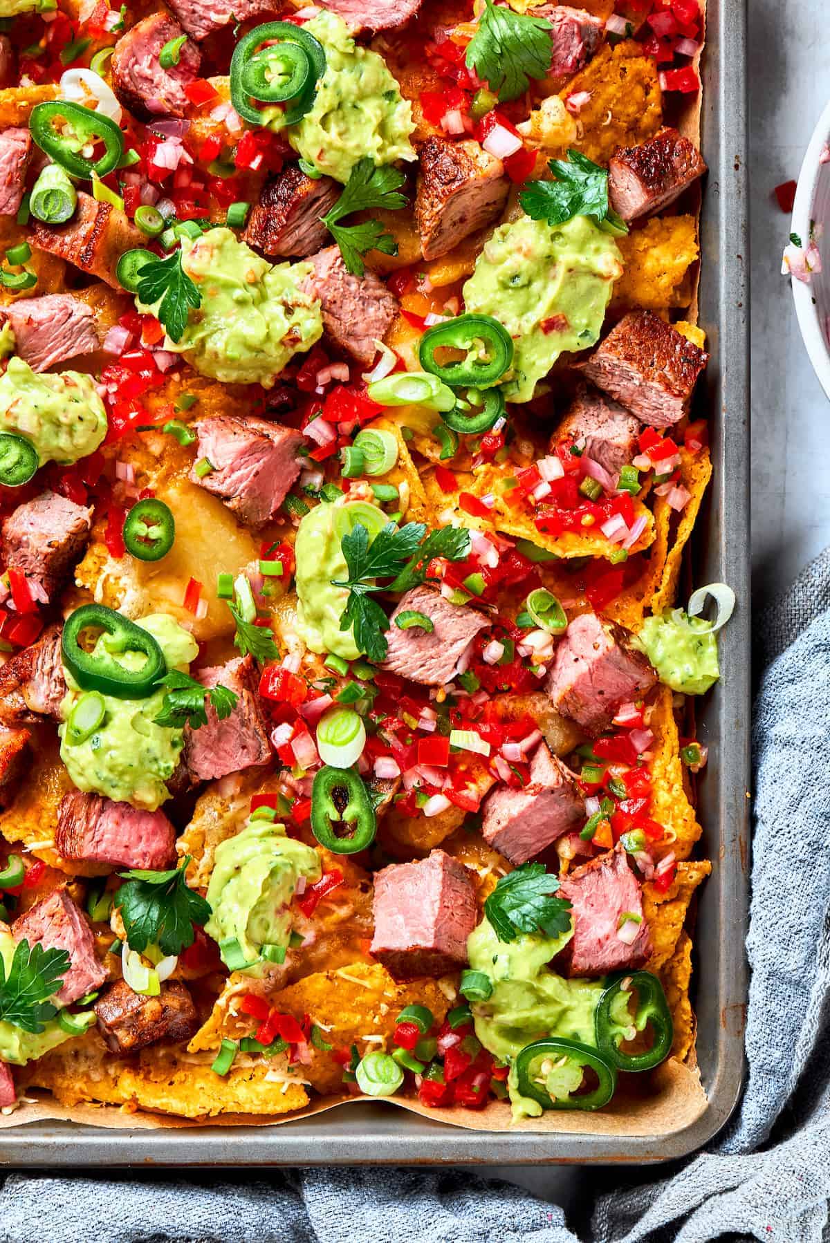 Weekly Meal Plan Nachos arranged on a baking sheet and topped with steak bites, pico de gallo, guacamole, and slices of jalapeno.