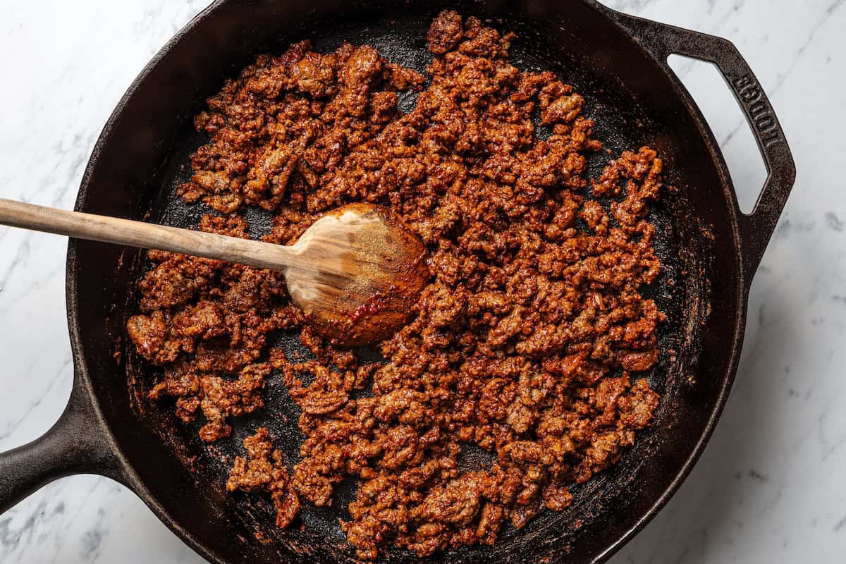 This Mexican-inspired taco pizza recipe has a crispy pizza crust topped with refried beans, taco meat, salsa, and your favorite taco toppings. Seasoned taco meat in a skillet.