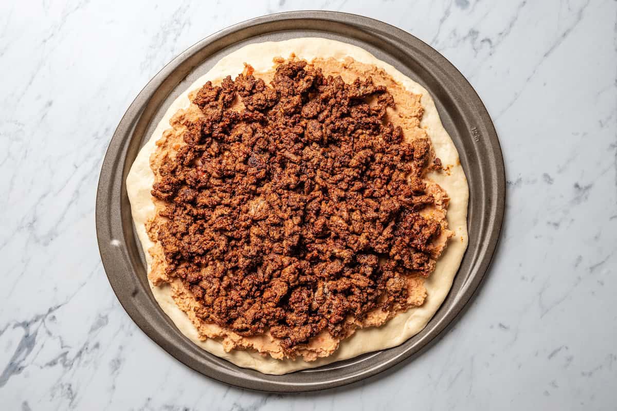 This Mexican-inspired taco pizza recipe has a crispy pizza crust topped with refried beans, taco meat, salsa, and your favorite taco toppings. Ground beef taco meat added to a pizza crust.