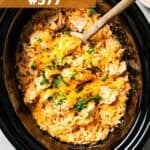 A wooden spoon stirring through chicken and rice in the slow cooker.