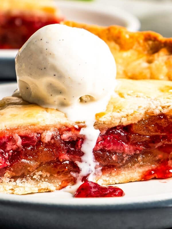 A slice of apple berry pie topped with a scoop of vanilla ice cream and served on a plate.