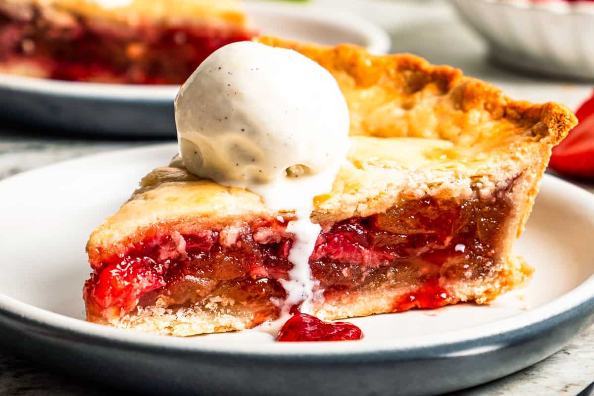 Apple berry pie is the perfect dessert to go from summer to fall! A cozy homemade apple pie bursting with fresh berries in a flaky pie crust. A slice of apple berry pie topped with a scoop of vanilla ice cream and served on a plate.