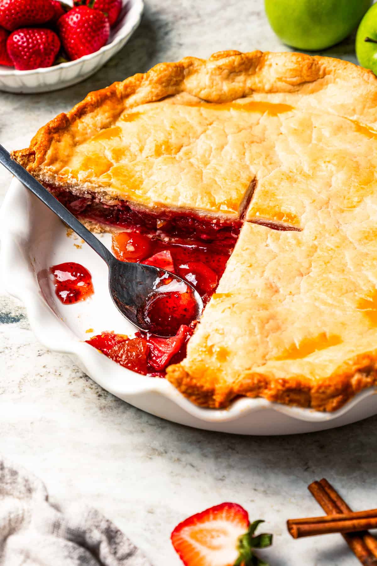Apple berry pie is the perfect dessert to go from summer to fall! A cozy homemade apple pie bursting with fresh berries in a flaky pie crust. Homemade apple berry pie in a pie plate with a spoon resting in an open space.