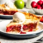 A slice of apple berry pie topped with a scoop of vanilla ice cream and served on a plate.