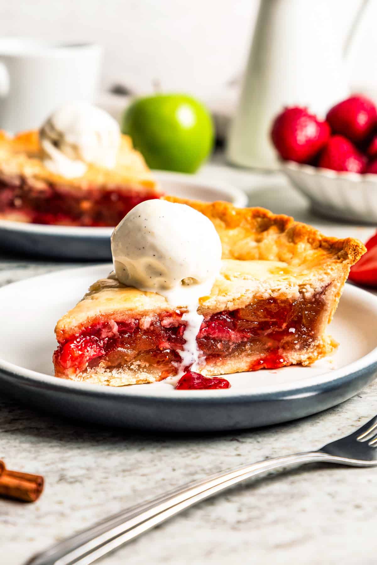 Apple berry pie is the perfect dessert to go from summer to fall! A cozy homemade apple pie bursting with fresh berries in a flaky pie crust. A slice of apple berry pie topped with a scoop of vanilla ice cream and served on a plate.