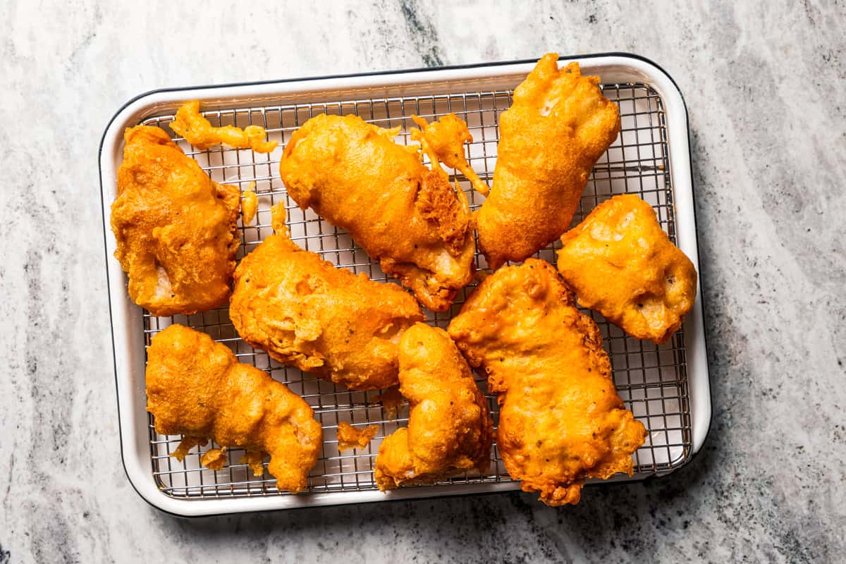 Make beer-battered fish with easy ingredients! This crispy, flaky fried white fish is perfect for tacos, pub-style fish and chips, and more. Fried beer battered fish draining on a wire rack.