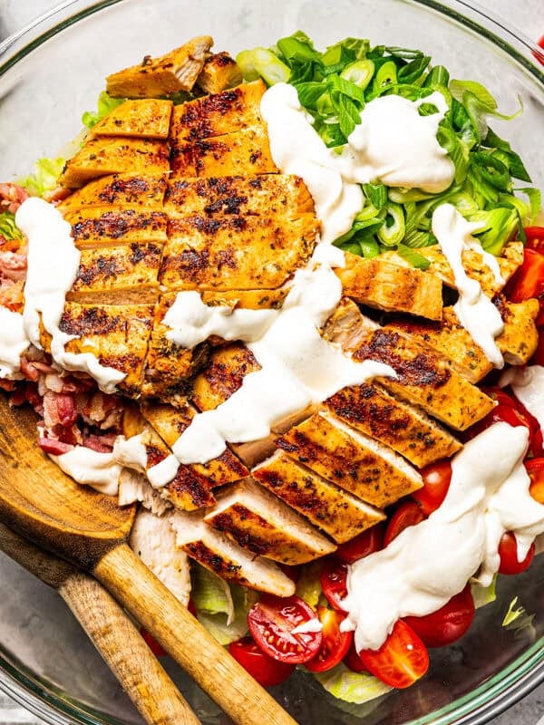 Creamy salad dressing drizzled over BLT chicken salad ingredients in a bowl.