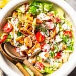 BLT grilled chicken salad in a bowl with salad tongs.