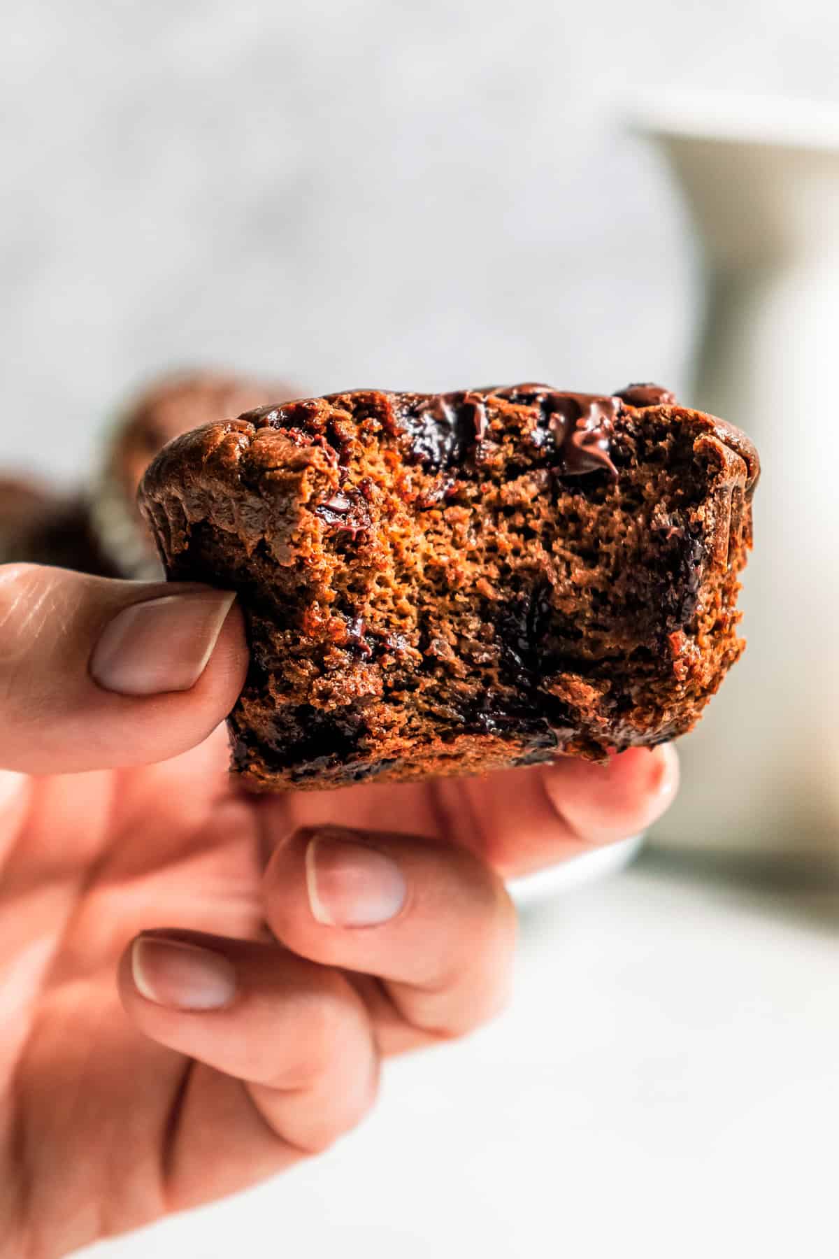 Chocolate protein muffins are moist, loaded with hidden veggies, and easy to make in the blender for a high-protein breakfast or meal prep. A hand holding up a chocolate protein muffin with a bite missing.