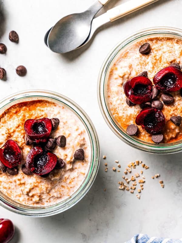 Steel cut oats in jars topped with fresh cherries, and with bowls of cherries and chocolate chips surrounding the jars.