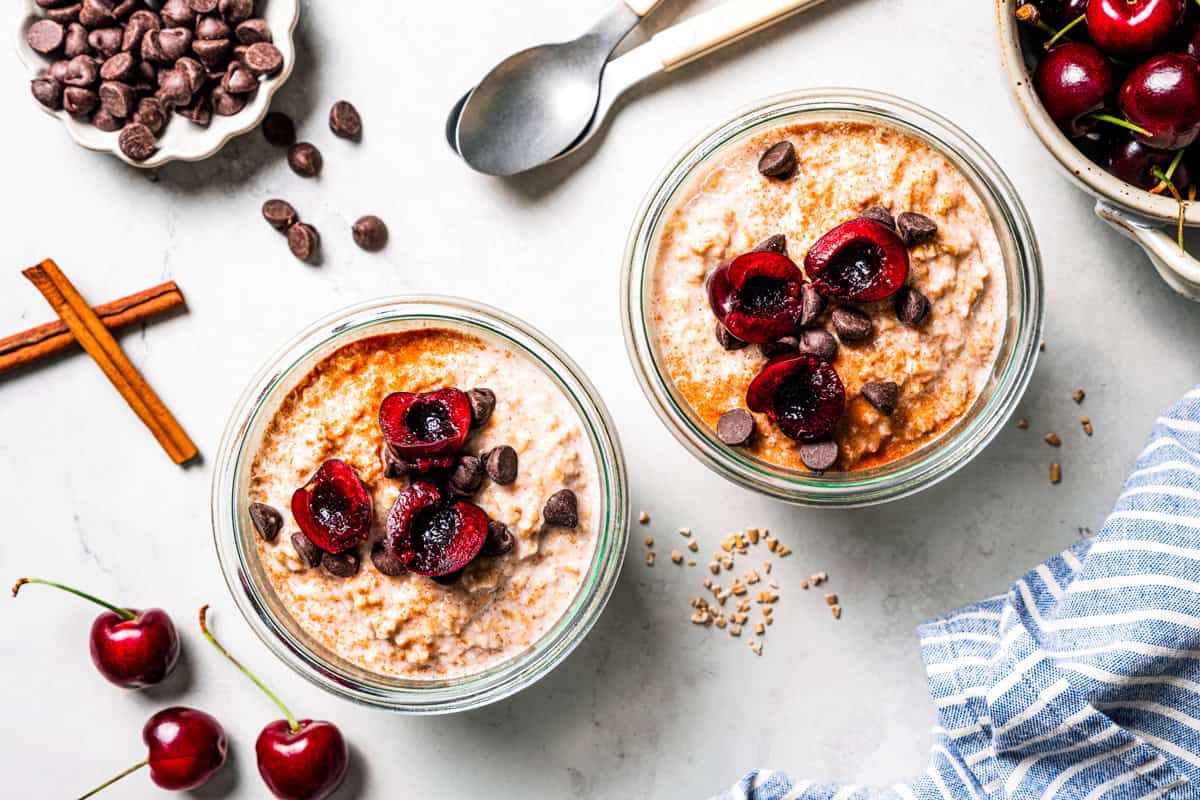 This easy overnight steel-cut oats recipe combines chewy oats, milk, vanilla, and cozy cinnamon into a delicious make-ahead breakfast. Steel cut oats in jars topped with fresh cherries, and with bowls of cherries and chocolate chips surrounding the jars.
