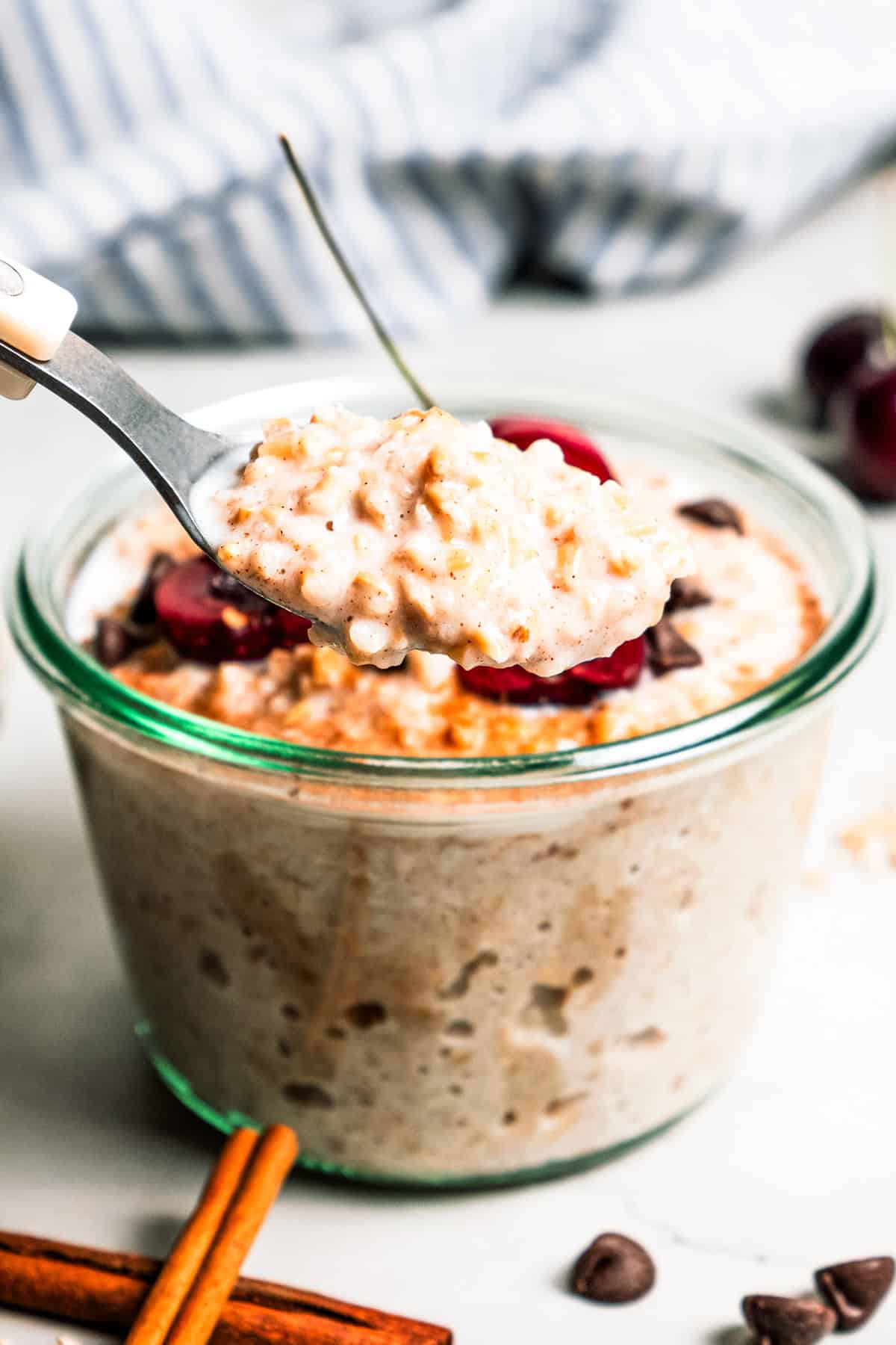 This easy overnight steel-cut oats recipe combines chewy oats, milk, vanilla, and cozy cinnamon into a delicious make-ahead breakfast. A spoon scooping overnight steel cut oats from a jar.