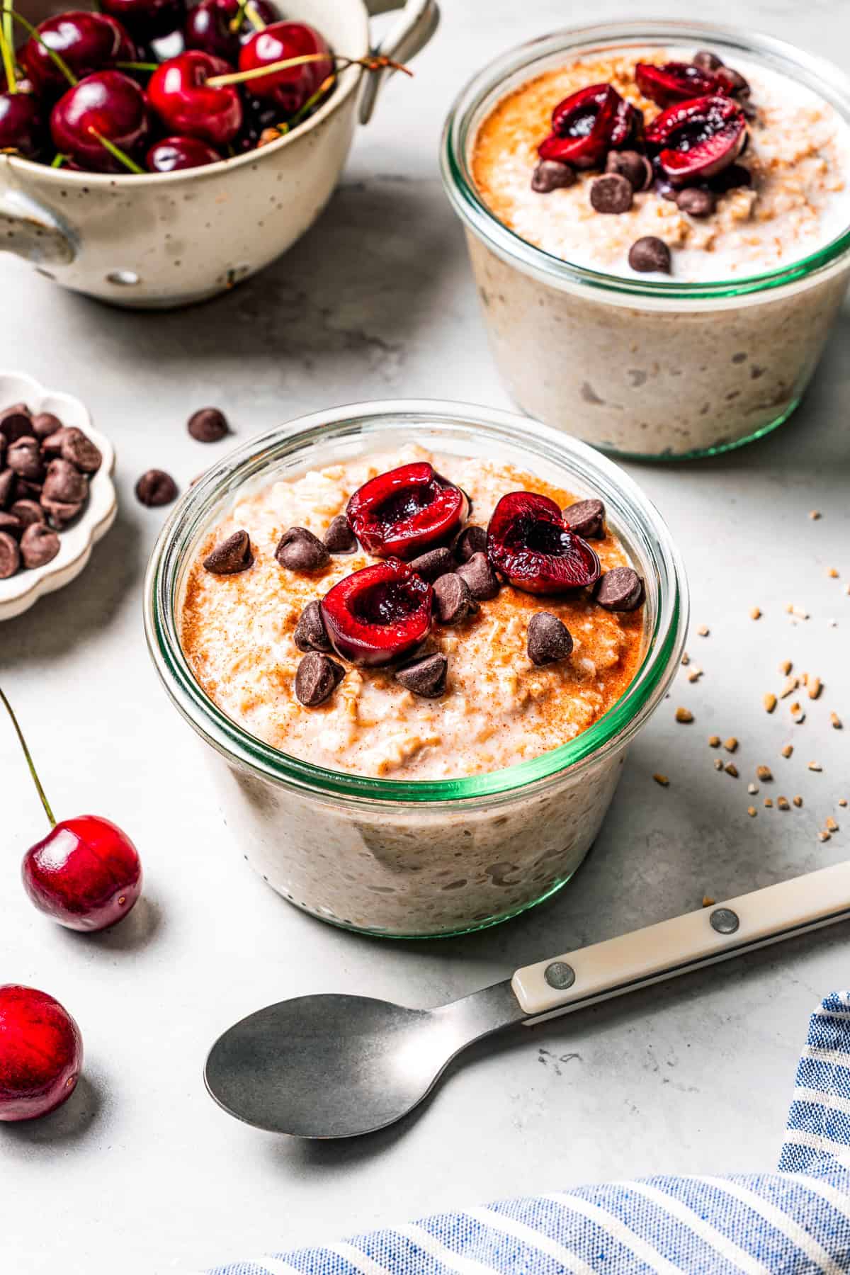 This easy overnight steel-cut oats recipe combines chewy oats, milk, vanilla, and cozy cinnamon into a delicious make-ahead breakfast. Overnight steel cut oats in jars topped with fresh cherries and chocolate chips.