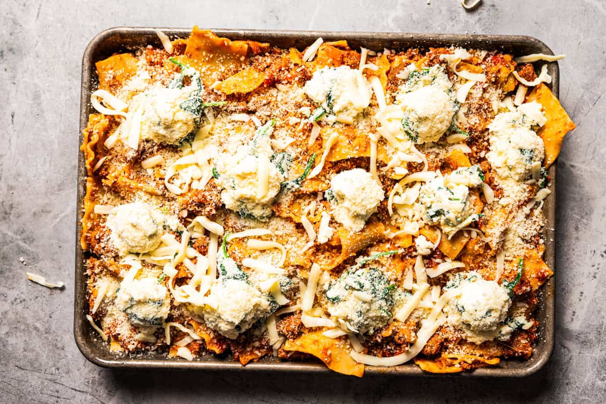 Sheet pan lasagna is a cheesy, delicious, golden-baked lasagna recipe with crispy edges and no layering required. Mix, dump, and bake! Assembled sheet pan lasagna ready for the oven.
