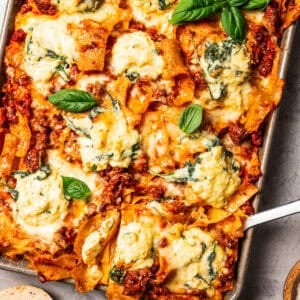 Overhead view of a cheesy sheet pan lasagna garnished with fresh basil leaves.
