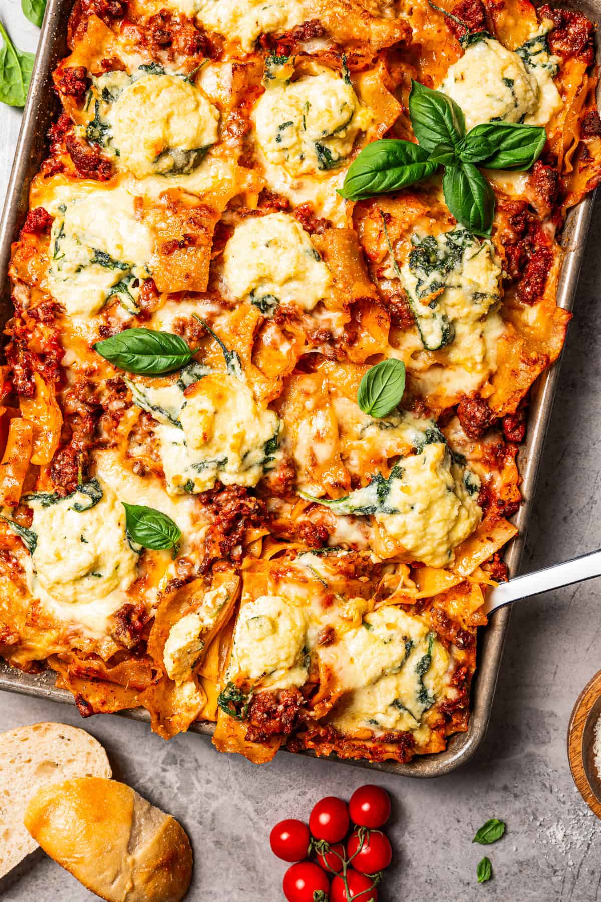 Sheet pan lasagna is a cheesy, delicious, golden-baked lasagna recipe with crispy edges and no layering required. Mix, dump, and bake! Overhead view of a cheesy sheet pan lasagna garnished with fresh basil leaves.