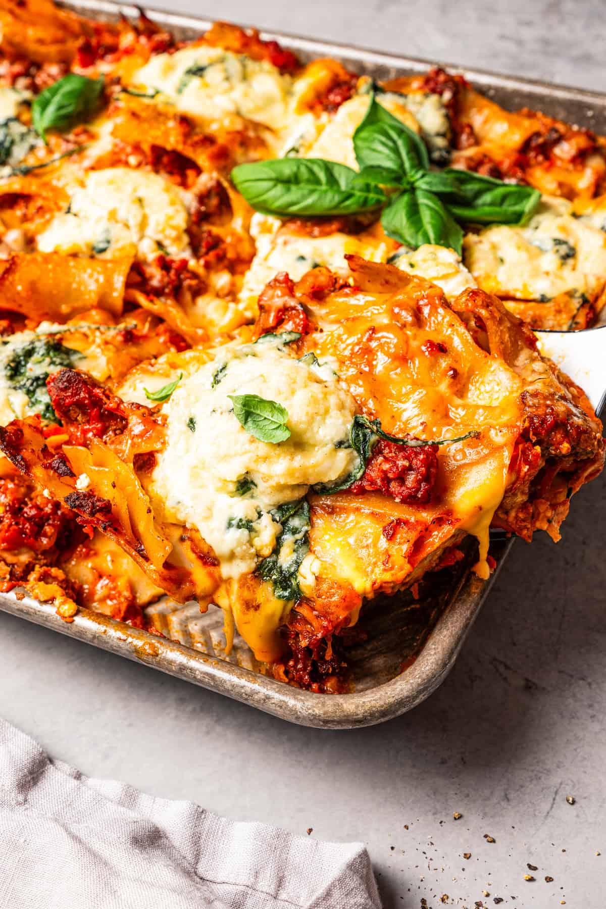 Sheet pan lasagna is a cheesy, delicious, golden-baked lasagna recipe with crispy edges and no layering required. Mix, dump, and bake! A slice of cheesy beef lasagna being lifted from a sheet pan.