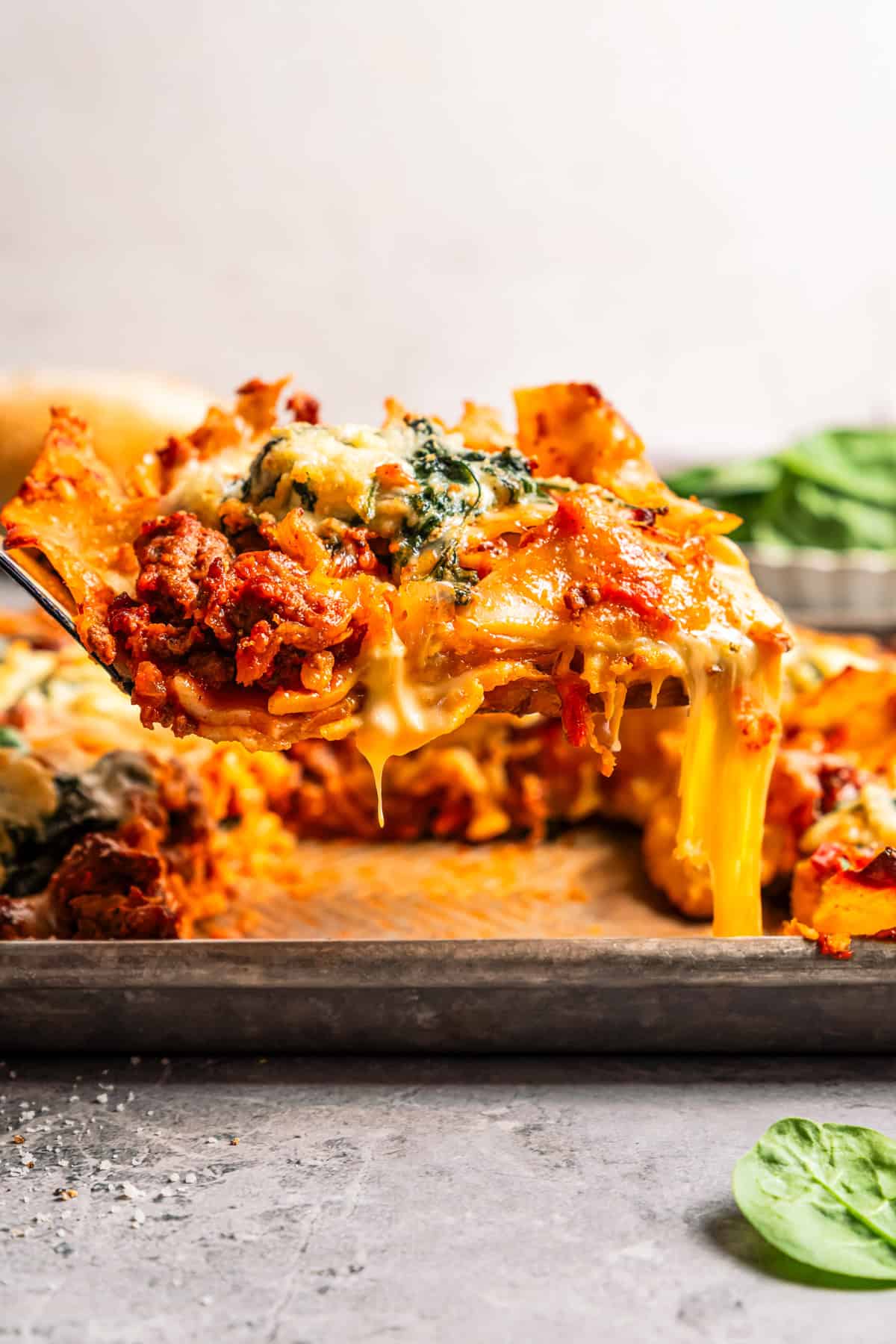 Sheet pan lasagna is a cheesy, delicious, golden-baked lasagna recipe with crispy edges and no layering required. Mix, dump, and bake! A slice of cheesy beef lasagna being lifted from a sheet pan.