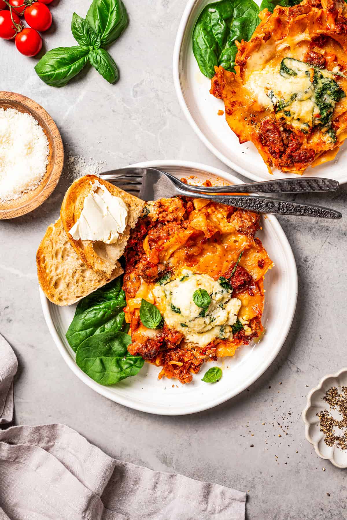 Sheet pan lasagna is a cheesy, delicious, golden-baked lasagna recipe with crispy edges and no layering required. Mix, dump, and bake! Two dinner plates with slices of lasagna served with crusty bread.