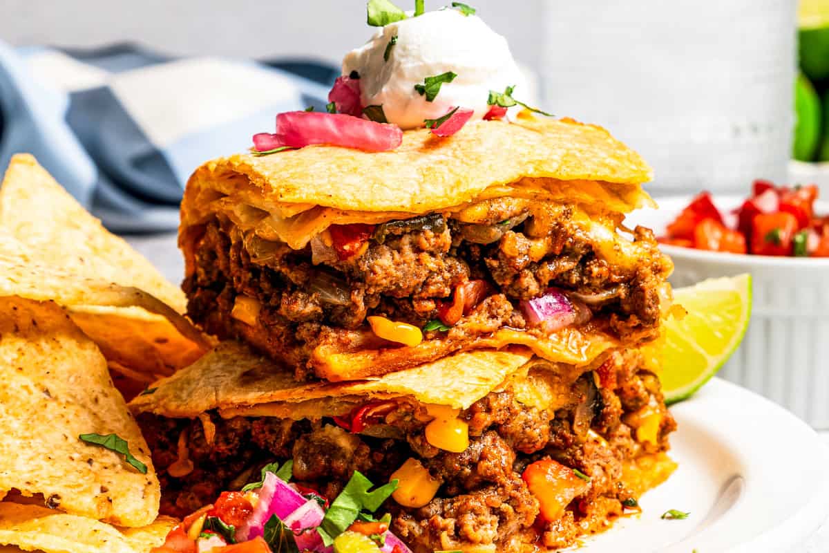 Baked sheet pan tacos are an easy way to make tacos for a crowd with crispy tortillas, seasoned ground beef, melty cheese, and pico de gallo. Close-up of sheet pan tacos made with flour tortillas, ground beef, cheese, corn, and peppers.