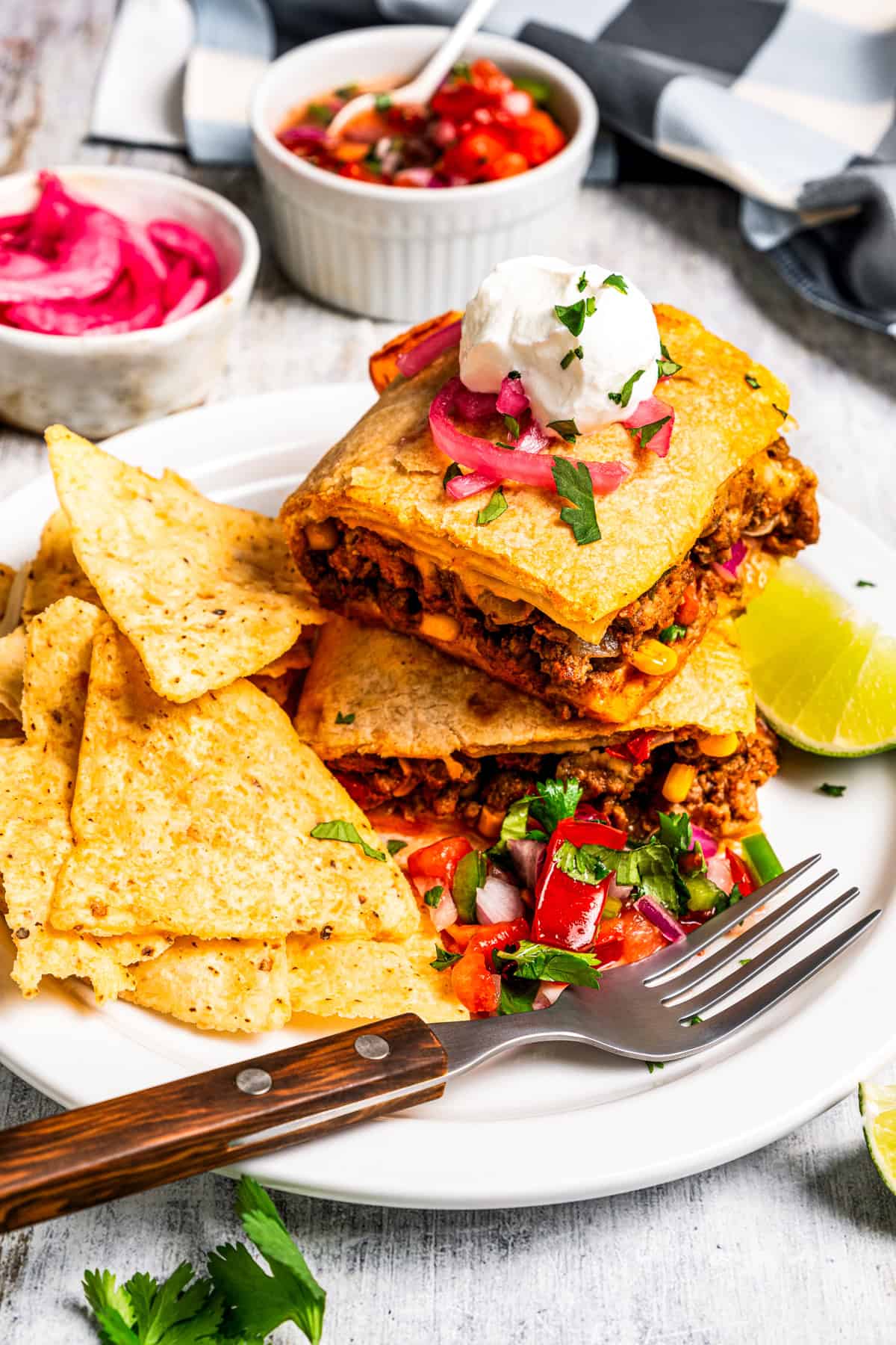 Baked sheet pan tacos are an easy way to make tacos for a crowd with crispy tortillas, seasoned ground beef, melty cheese, and pico de gallo. Sheet pan tacos served on a plate next to pico de gallo and tortilla chips.