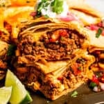 Stacked sheet pan tacos with crispy tortillas, filled with ground beef, melted cheese, and vegetables, topped with sour cream and fresh cilantro.