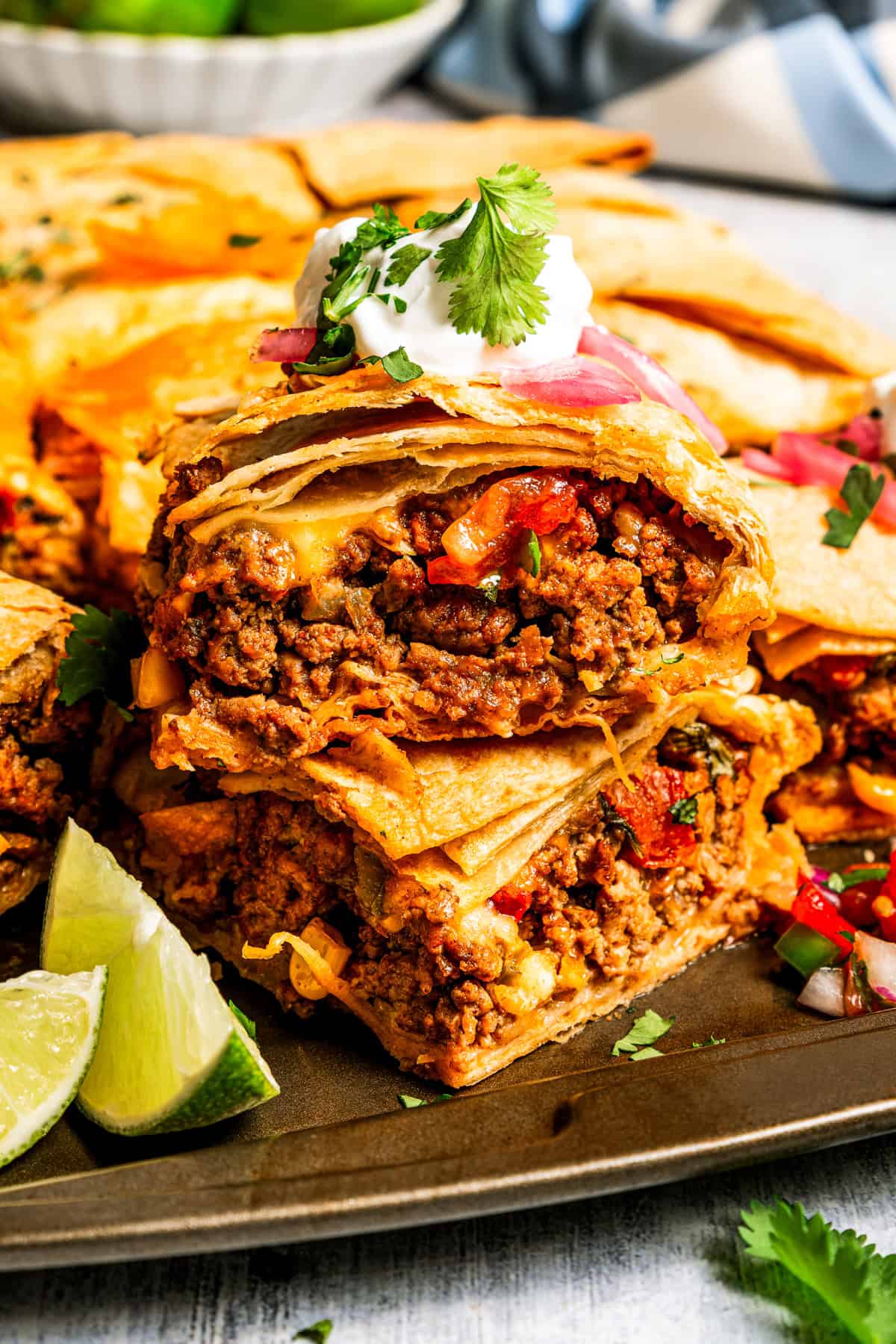Baked sheet pan tacos are an easy way to make tacos for a crowd with crispy tortillas, seasoned ground beef, melty cheese, and pico de gallo. Stacked sheet pan tacos with crispy tortillas, filled with ground beef, melted cheese, and vegetables, topped with sour cream and fresh cilantro.