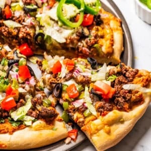 A slice of taco pizza partially removed from the rest of the pizza on a pan.