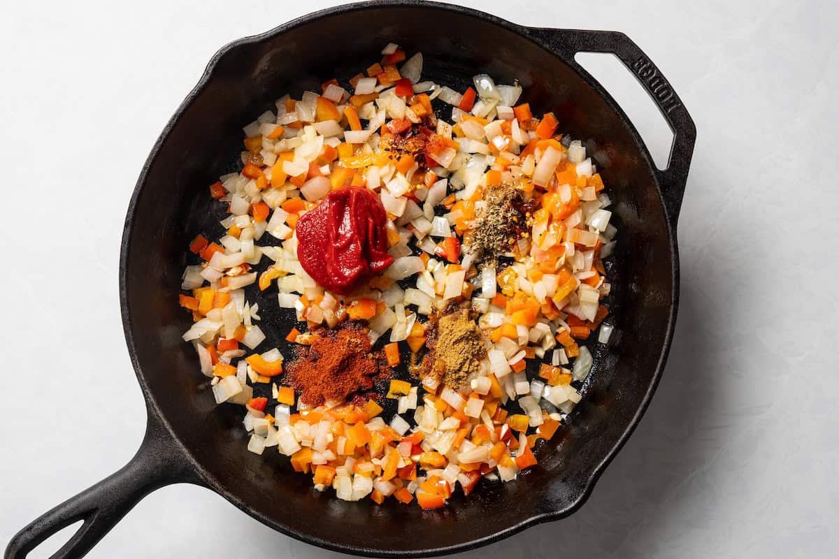 Tomato paste and spices added to sautéed veggies in a skillet.