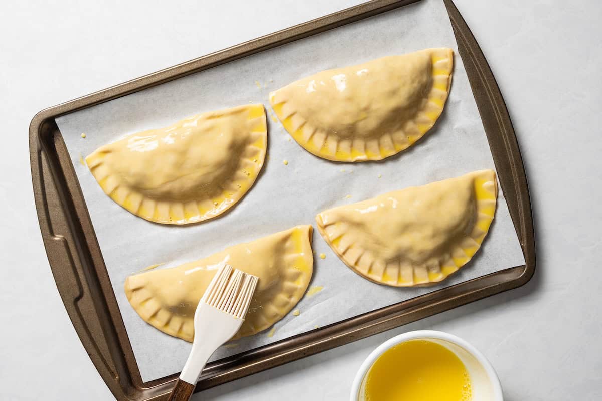Brushing unbaked chicken empanadas with egg wash.