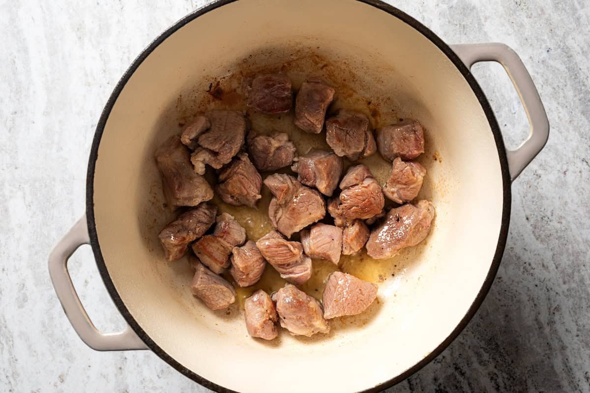 This slow-braised pork ragu recipe cooks for hours in the oven until fall-apart tender and ready to shred into a rich, flavorful meat sauce. Seared pork shoulder pieces in a large pot.