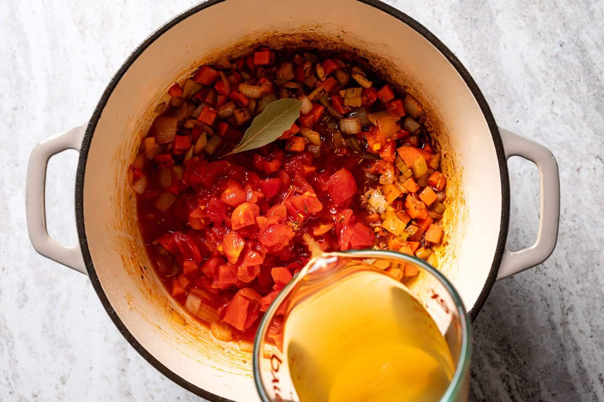 This slow-braised pork ragu recipe cooks for hours in the oven until fall-apart tender and ready to shred into a rich, flavorful meat sauce. Pouring chicken stock over the rest of the ragu ingredients in a pot.
