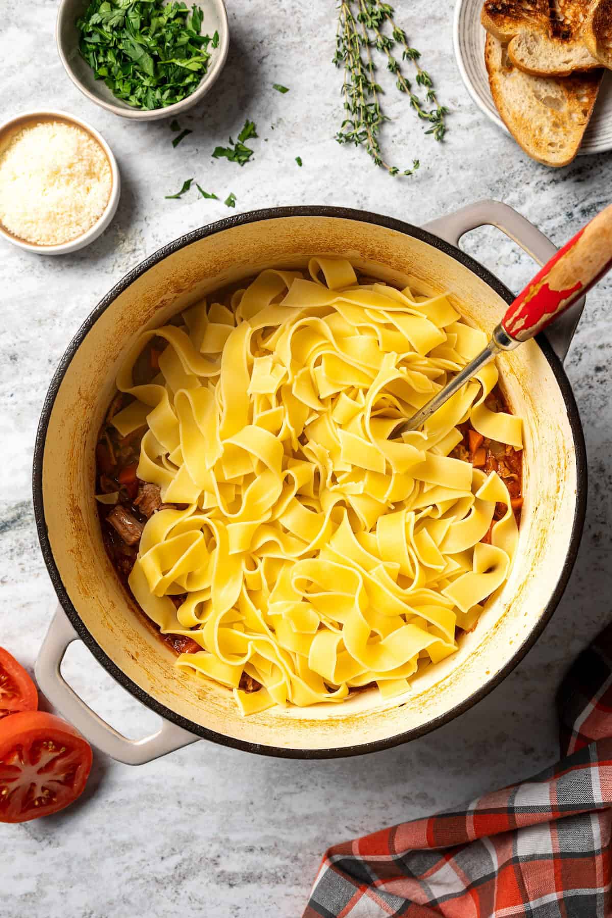 This slow-braised pork ragu recipe cooks for hours in the oven until fall-apart tender and ready to shred into a rich, flavorful meat sauce. Pappardelle noodles added to pork ragu in a large pot.