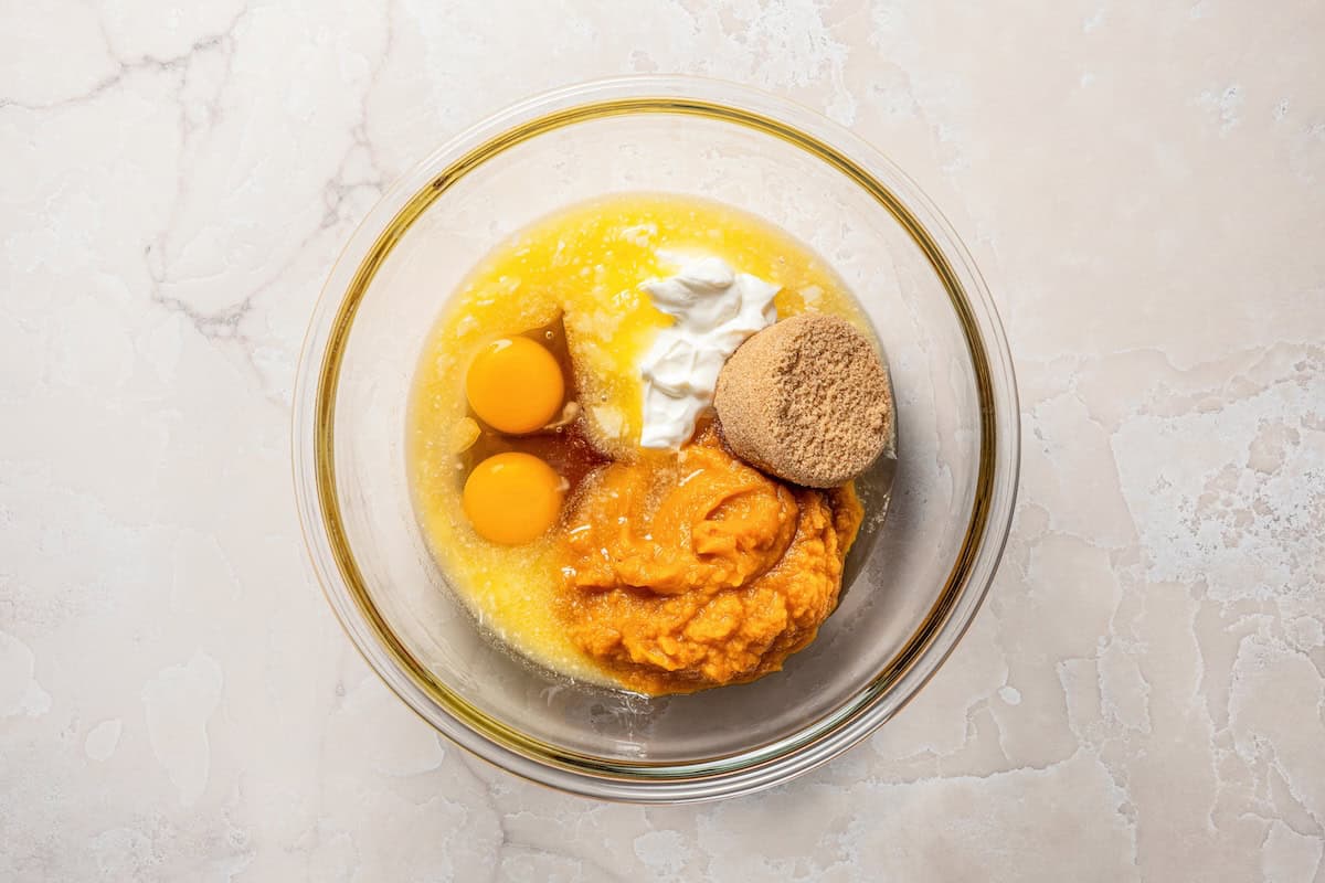 These pumpkin cream cheese muffins are moist, spiced pumpkin muffins swirled with cream cheese filling and topped with toasted pecans. Wet pumpkin muffins ingredients combined in a bowl.