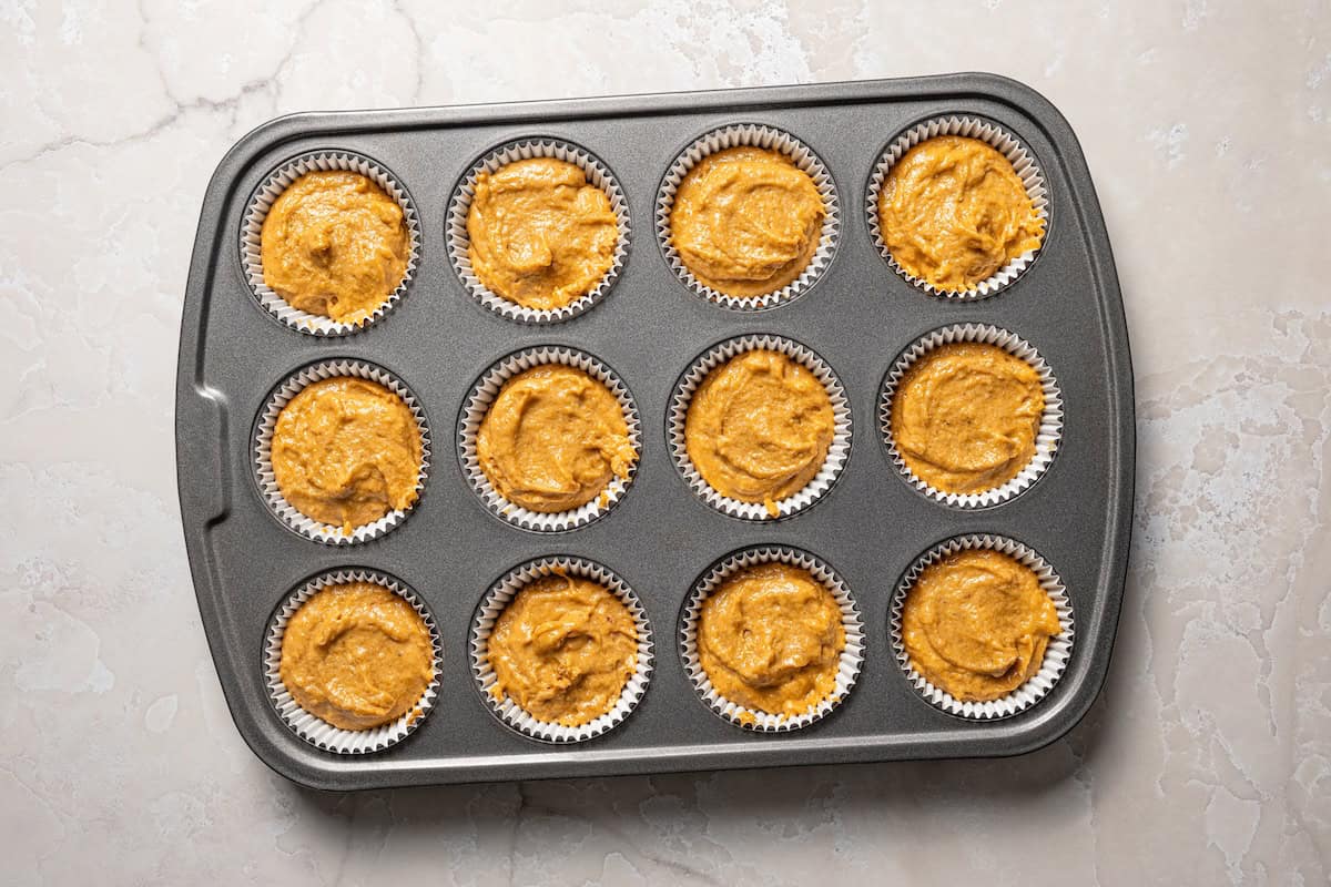 These pumpkin cream cheese muffins are moist, spiced pumpkin muffins swirled with cream cheese filling and topped with toasted pecans. A muffin pan filled with pumpkin muffin batter.