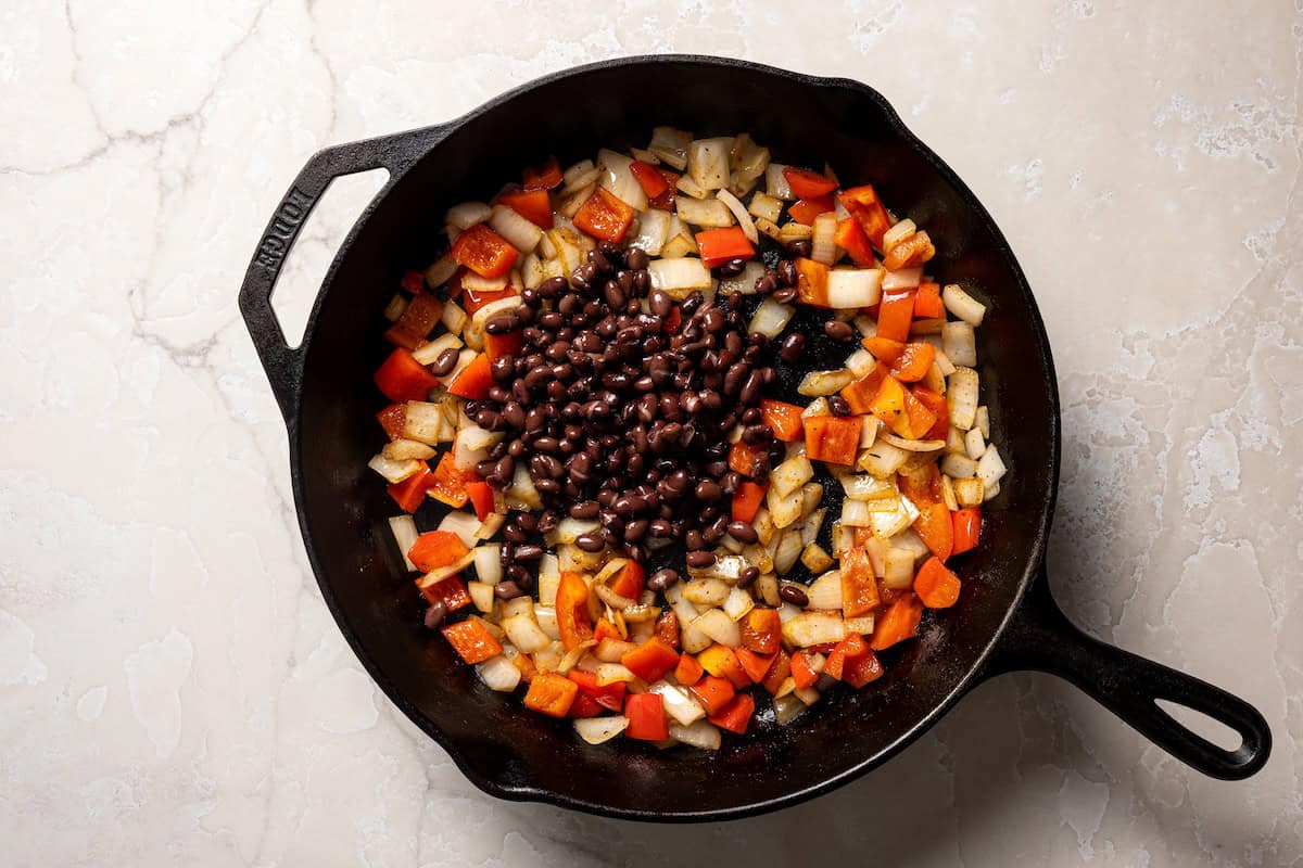 Black beans added to sautéed veggies in a skillet.