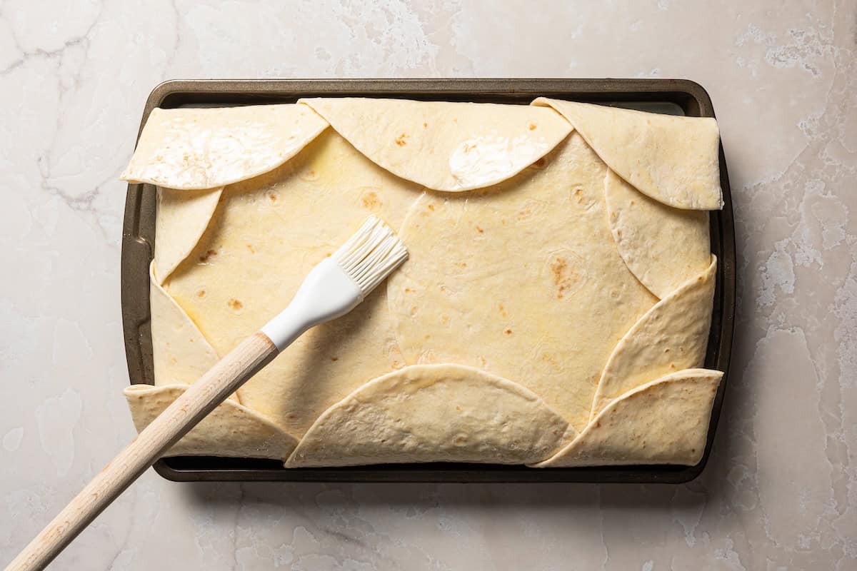 Brushing unbaked sheet pan quesadillas with melted butter.