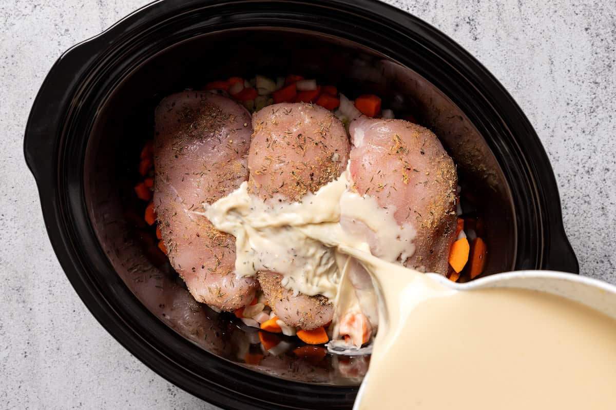 This slow cooker chicken and dumplings recipe is a cozy, creamy chicken stew loaded with homemade biscuit dumplings. All cooked in one pot! Pouring the creamy sauce over the chicken in the crock pot.