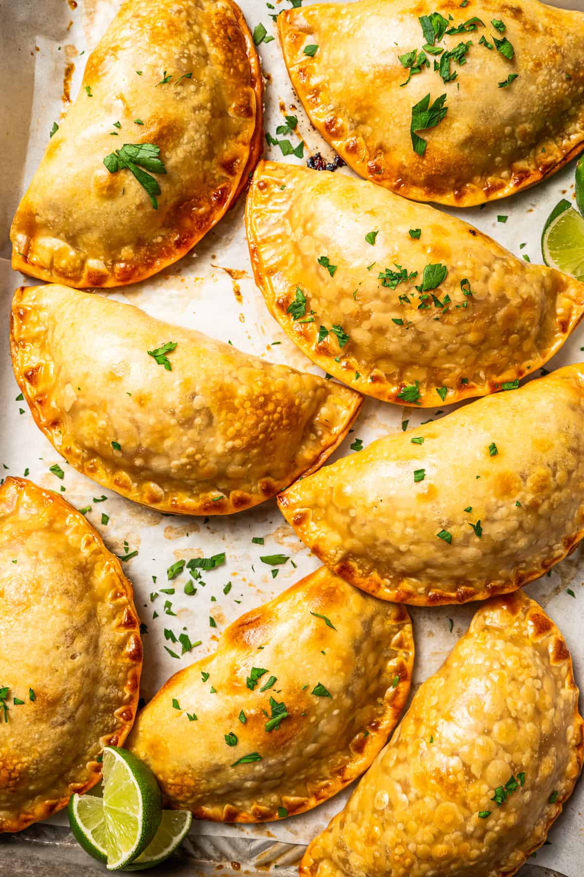 Close up of cooked empanadas arranged on a white surface.