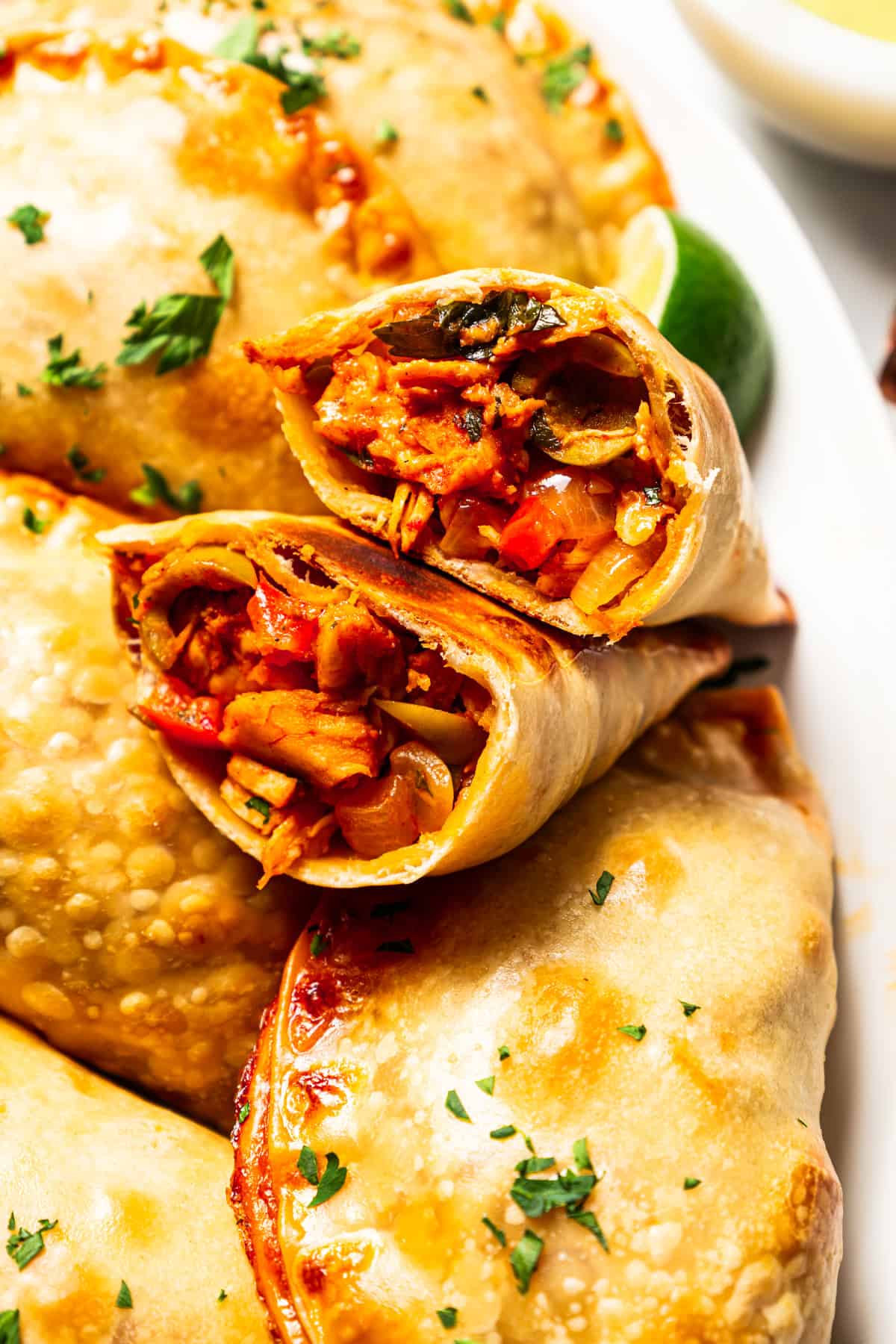 Close up of homemade chicken empanadas on a plate with one broken in half to reveal the filling.